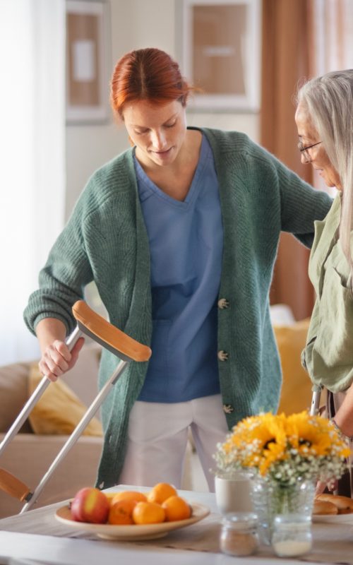 Nurse helping senior woman with walking after leg injury.